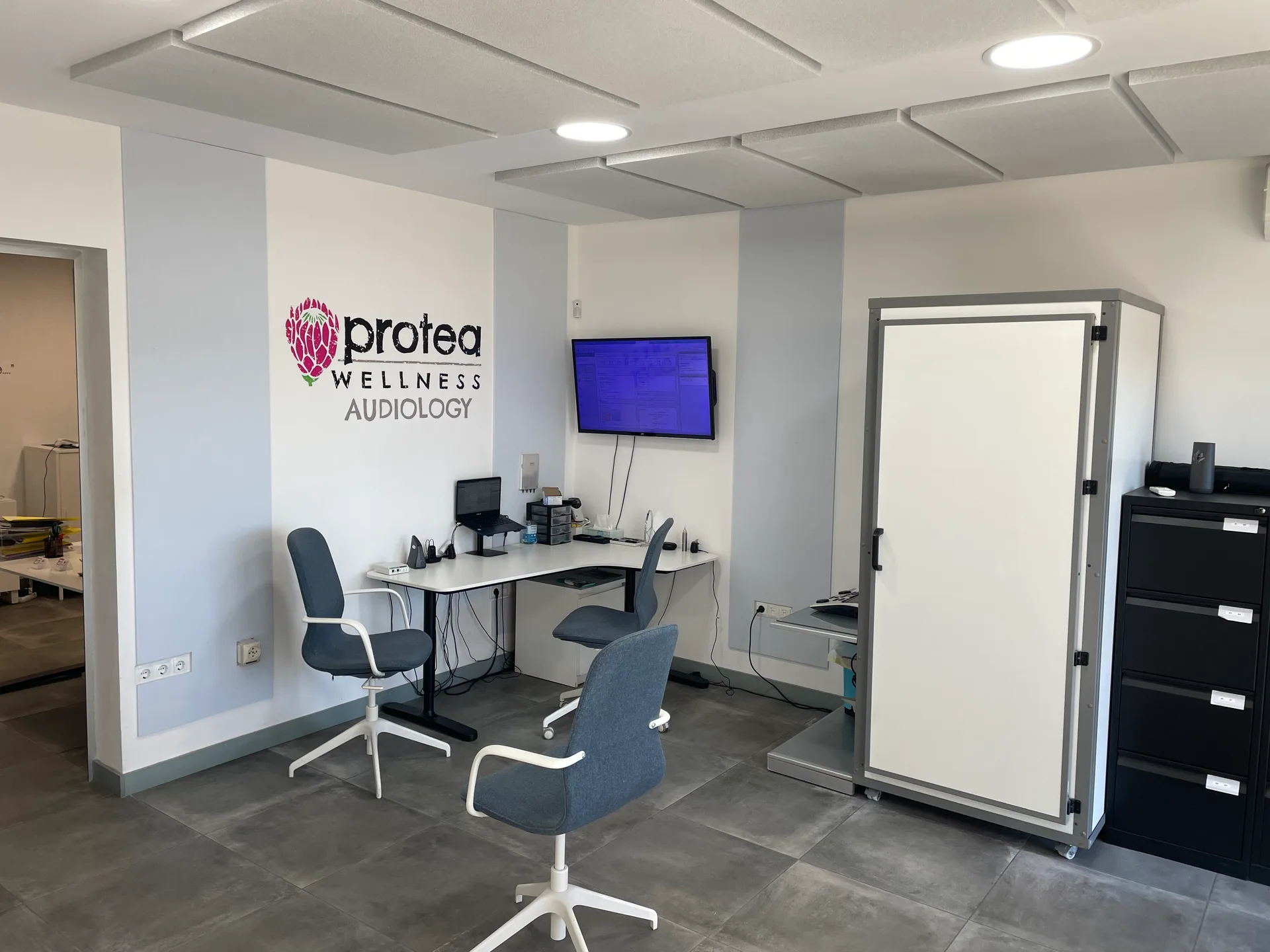 The Protea Wellness Audiology clinic - Ciudad Quesada consulting room with logo wall and audiometric booth